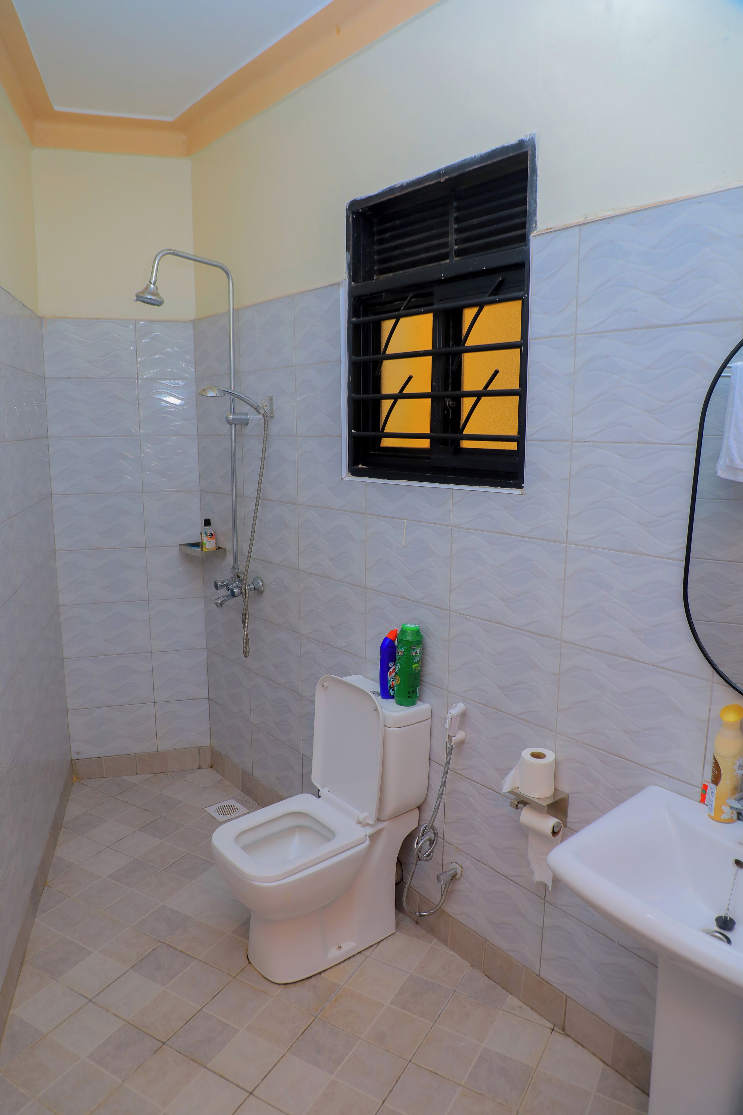 A bathroom with a toilet, sink, shower, and a window with a black frame.