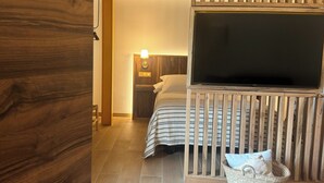 A bedroom with a bed, a TV, a nightstand, and a wooden ceiling structure. - ARENAS SUITES APARTAMENTOS (Potes)