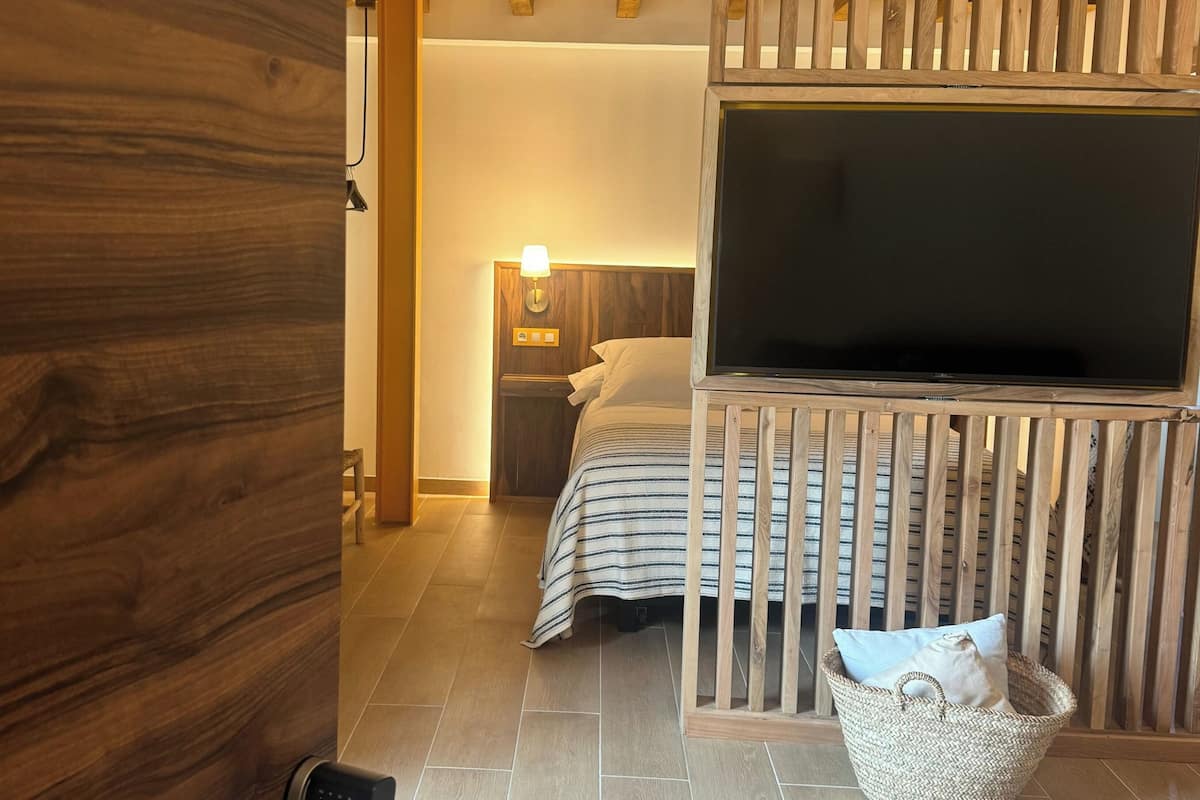 A bedroom with a bed, a TV, a nightstand, and a wooden ceiling structure.