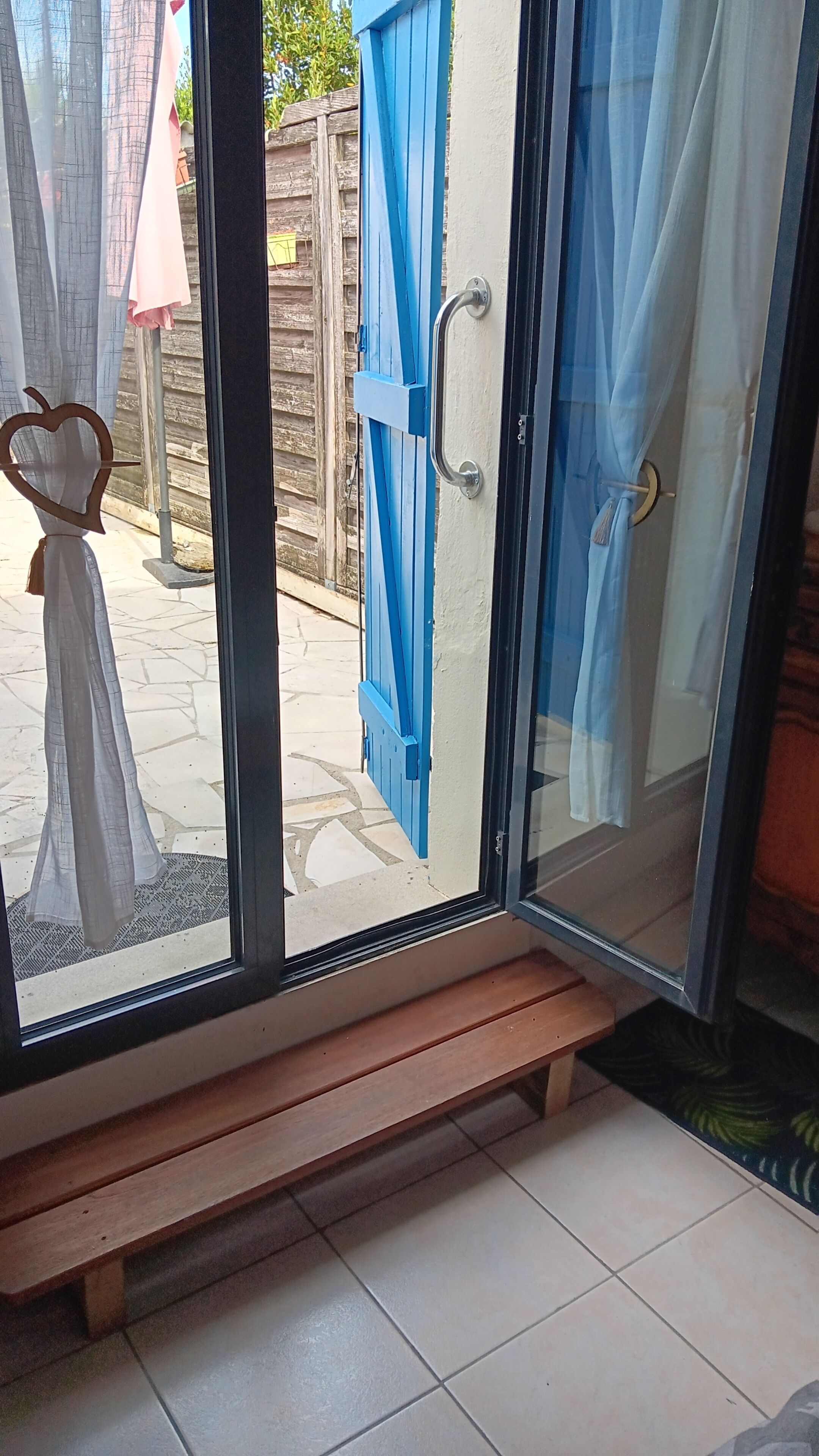A room with a bench, a sliding glass door with blue curtains, and a view of the outside.