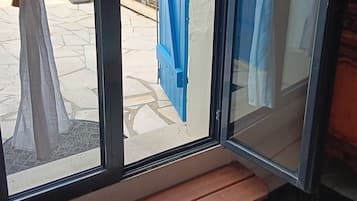 A room with a bench, a sliding glass door with blue curtains, and a view of the outside.