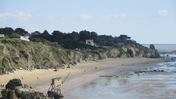 Une plage avec un poste de surveillance pour les sauveteurs, des affleurements rocheux et des maisons construites sur une falaise.