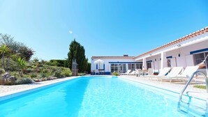 A clear blue swimming pool with lounge chairs and a building with a tiled roof in the background. - Ocean Whisper-spectacular villa on Portugal's west coast (Aljezur)