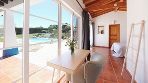 A room with a wooden ceiling, a large window, a table with a vase, a chair, and a bed with a striped blanket. - Ocean Whisper-spectacular villa on Portugal's west coast (Aljezur)