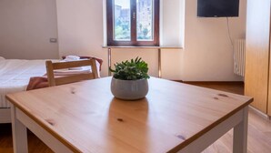 Una habitación con una mesa de madera, una silla, una cama, un ventanal y un televisor montado en la pared.