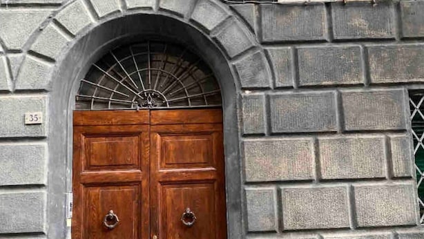 Puerta doble de madera con una celosía metálica encima, ubicada en un muro de piedra donde se aprecia el número '35' a la izquierda.