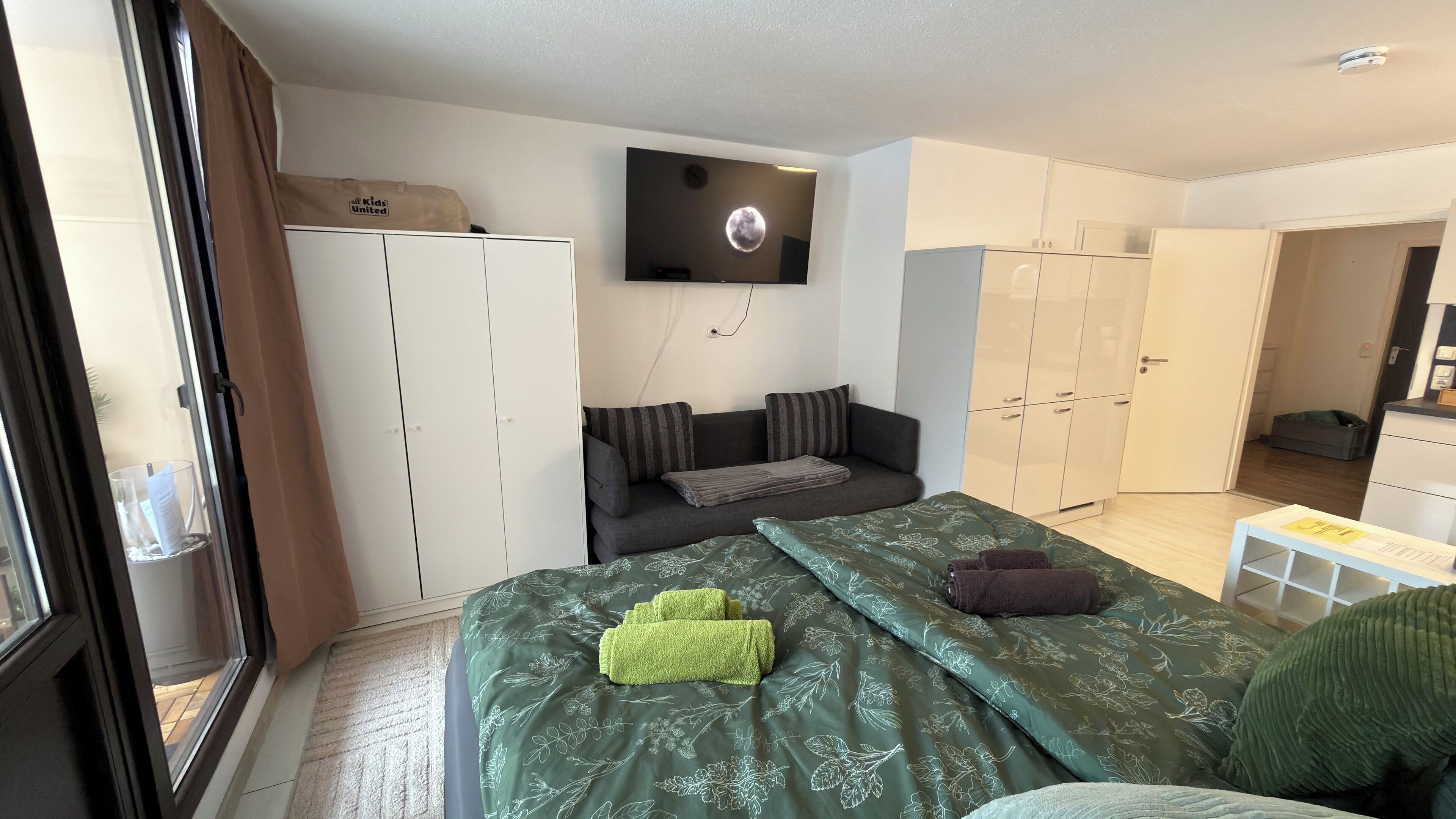 Ein modernes Schlafzimmer mit einem Bett, einer Couch, einem Fernseher und einem Kleiderschrank.