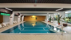 An indoor swimming pool with clear water, surrounded by lounge chairs and potted plants. - Apartment Luna, Sankt Englmar (Sankt Englmar)