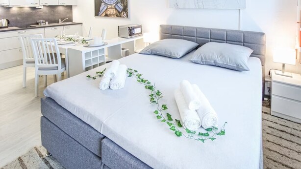 A modern hotel room with a neatly made bed, a dining area with a table and chairs, and a kitchen in the background. - Apartment Luna, Sankt Englmar (Sankt Englmar)