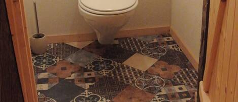Un baño pequeño y estrecho con inodoro, dispensador de papel higiénico y suelo de baldosas con diseño.