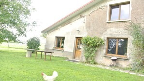 A rustic house with a grassy yard, a wooden door, and a window with a wooden frame. - Spacious cozy and pet friendly Gîte (6pers with 3 bdrms/2 baths/3 toilets). (Claudon)