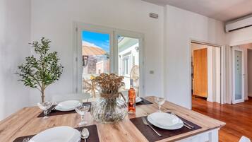 A dining area with a wooden table set for four, a potted plant, and a vase with dried flowers.