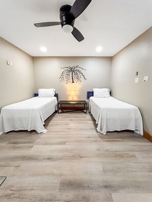 A hotel room with two single beds, a ceiling fan, a wall-mounted lamp, and a wooden floor. - Sunrise Breeze: waterfront escape with peaceful views and easy coastal living (Rockport)