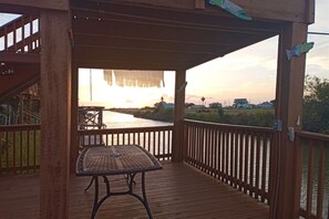 A wooden deck with a table and chairs, overlooking a body of water and a distant shoreline. - Sunrise Breeze: waterfront escape with peaceful views and easy coastal living (Rockport)