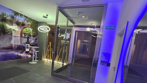 Entrada de hotel con puerta de vidrio, un letrero que indica 'SALIDA' y una pantalla digital.