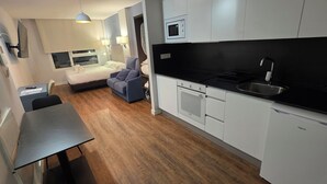 Cocina compacta con armarios blancos, encimera negra y microondas integrado.