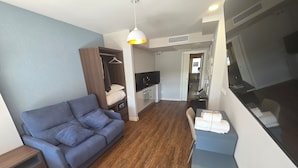 Una sala moderna con un sofá azul, un armario de madera, una zona de comedor con una mesa y sillas, y una kitchenette.