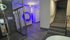 Un moderno vestíbulo de hotel con entrada de vidrio, un mostrador de recepción, una escalera y una pared iluminada en azul.