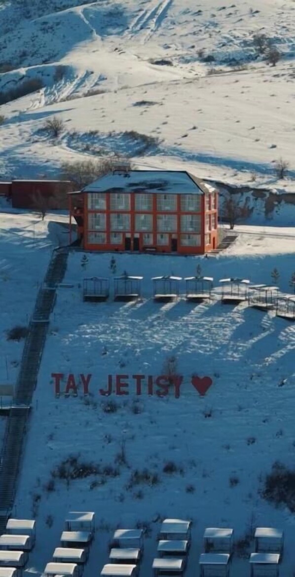 A red building with a glass facade, surrounded by snow-covered ground and parked vehicles.