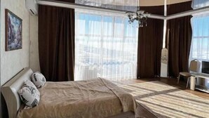 A modern hotel room with a large bed, a seating area, and a view of the city. - Tau Zhetysu (Yepkindi)