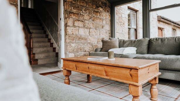 A cozy living room with a stone wall, a wooden coffee table, and a grey sofa.