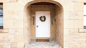 A stone entrance with a white door, a wreath, and a herringbone-patterned stone floor.