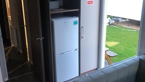 Ein Zimmer mit grauem Sofa, einem weißen Kühlschrank und einer Schiebetür zu einem Außenbereich mit Picknicktisch.