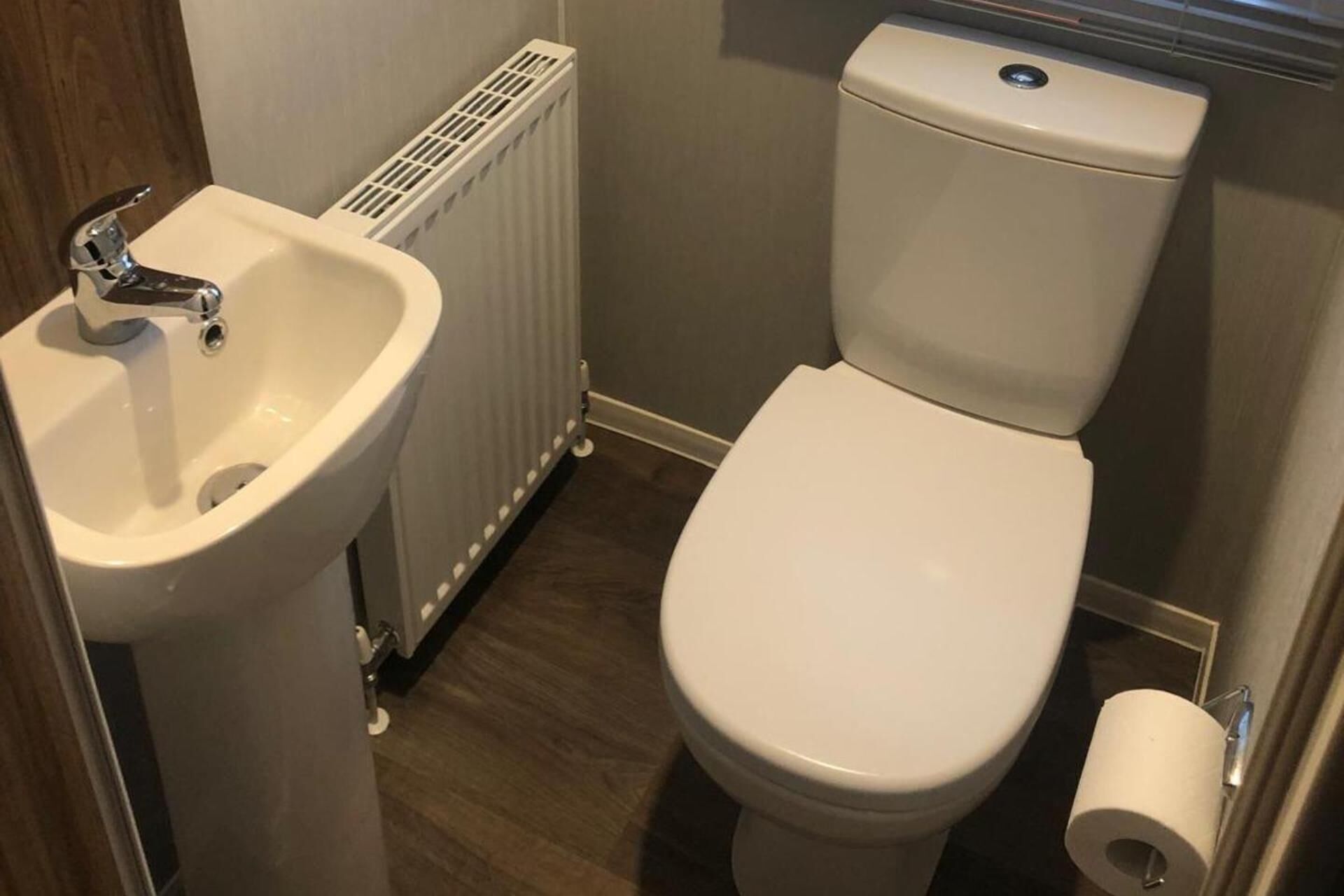 Un baño pequeño con un lavamanos, inodoro y radiador blancos.