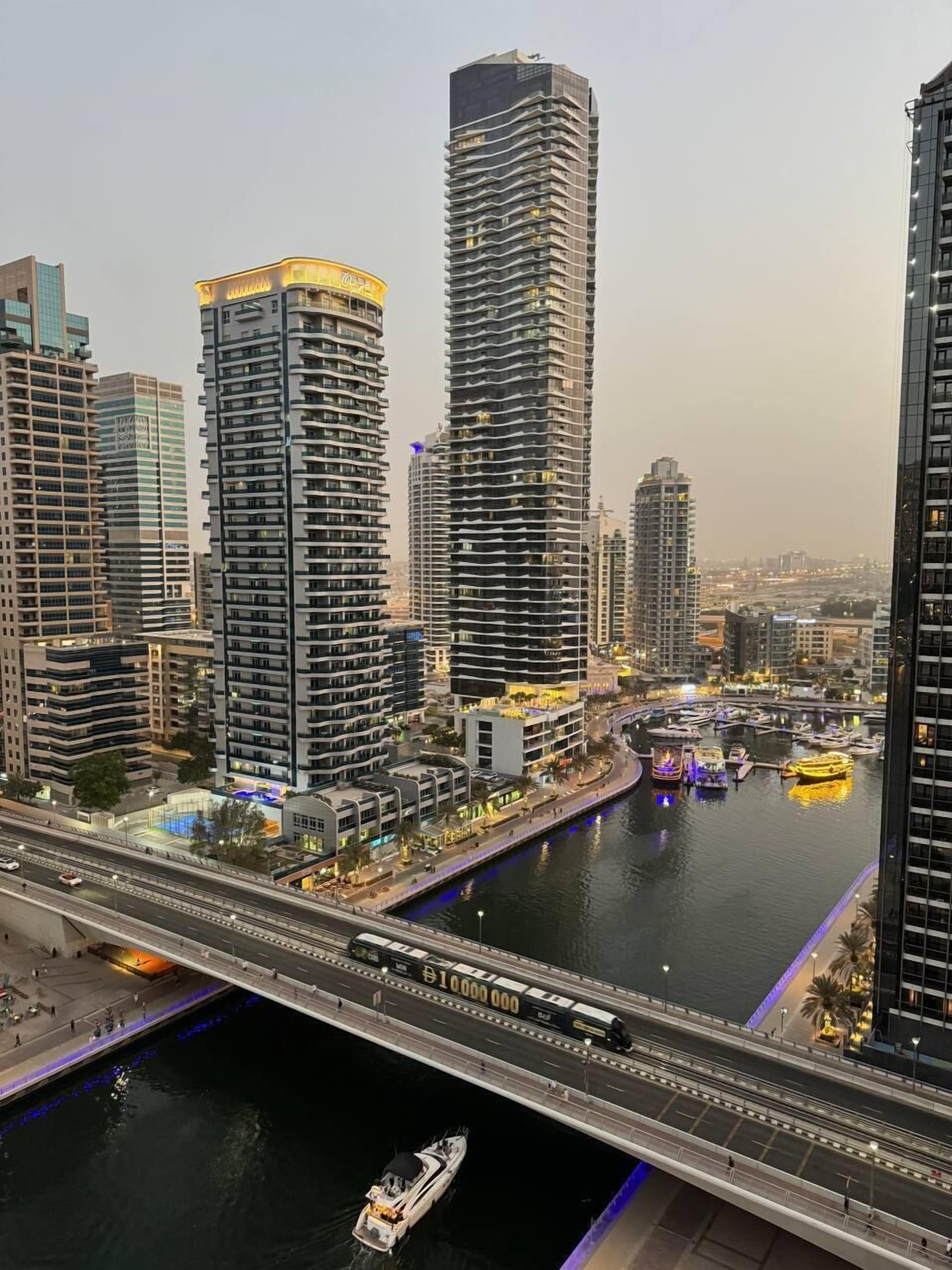 A high-rise building with a modern architectural design, situated next to a river with a bridge crossing over it.