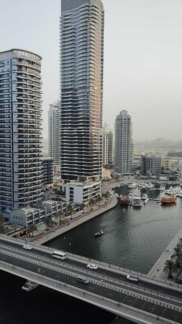 A high-rise building with a curved facade, a river with boats, and a bridge with vehicles. - Lyo hostel Marina Whraf 1 (Dubai)