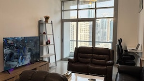 A modern living room with a large TV, leather sofas, a coffee table, and a view of tall buildings through large windows. - Lyo hostel Marina Whraf 1 (Dubai)