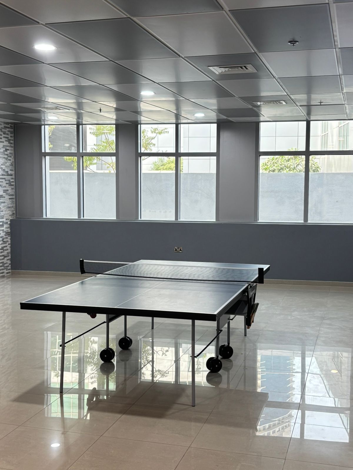 En rummelig stue med et pingpongbord, store vinduer og et flisegulv.
