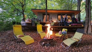 Un espace extérieur rustique aménagé avec des sièges, un foyer et entouré de chaises jaunes, le tout abrité par une structure en bois.