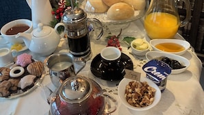 Une table dressée avec divers aliments pour le petit-déjeuner, notamment des viennoiseries, des boissons et des condiments, avec une bibliothèque en arrière-plan.