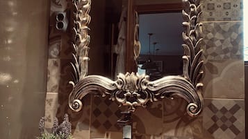 Un baño con un espejo grande y ornamentado, un lavabo de piedra y un mueble de tocador de madera.