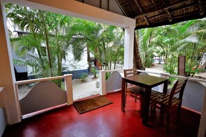A covered outdoor seating area with a table and chairs, surrounded by lush green palm trees. - Temple Garden (Canacona)