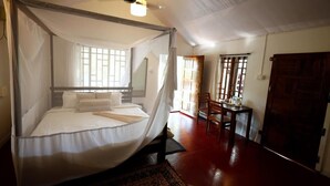 A bedroom with a bed under a mosquito net, a wooden chair, a table, and a door. - Temple Garden (Canacona)