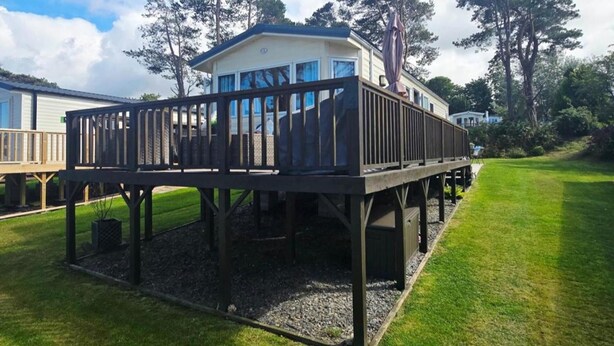 Una casa móvil con terraza, rodeada de césped y árboles.