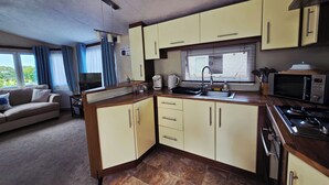 Cocina compacta con lavamanos, microondas y estufa. En la zona de estar contigua, hay una mesa de comedor y un sofá.