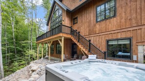 Una baita di legno con vasca idromassaggio, area salotto esterna e una scala che conduce a un patio.