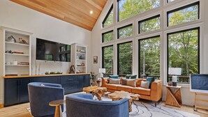 Un'ampia zona giorno con una grande finestra, un soffitto in legno e un moderno divano.