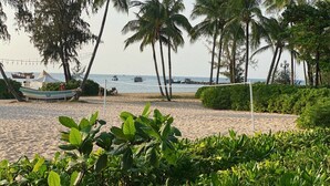 A beach with palm trees, a volleyball net, and boats in the water. - V&T Hotel Phu Quoc (Phu Quoc)