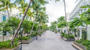 A wide, paved pathway flanked by palm trees and planters, leading to a building with white walls and green shutters. - V&T Hotel Phu Quoc (Phu Quoc)