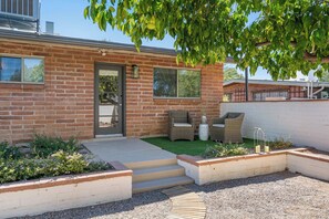 Ein Ziegelhaus mit Haustür, Stufen zu einer Veranda, Gartenmöbel und einem Garten.