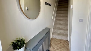 A hallway with a round mirror, a radiator, a potted plant, a staircase, and a hanging light fixture.
