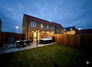 Un jardin à l’arrière d’une maison, avec une terrasse, un jacuzzi et une clôture en bois.