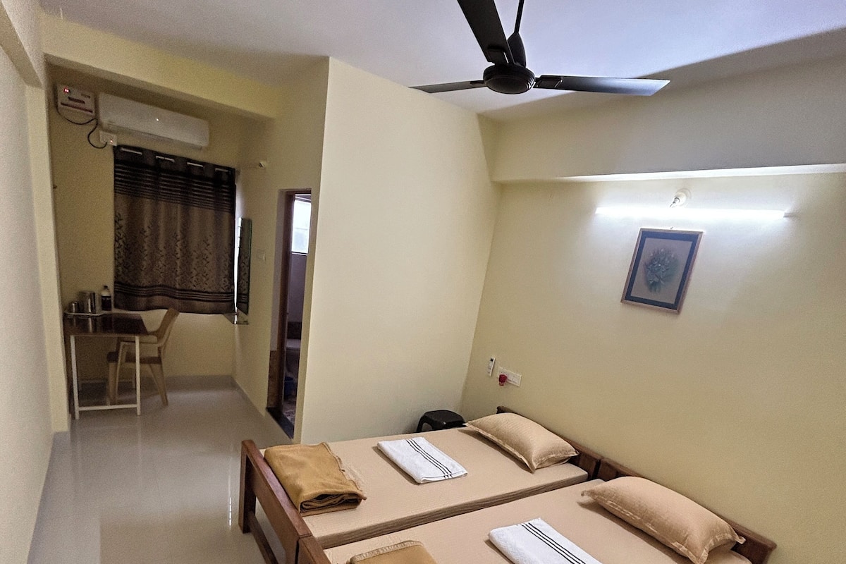 A hotel room with two beds, a desk, and a ceiling fan.