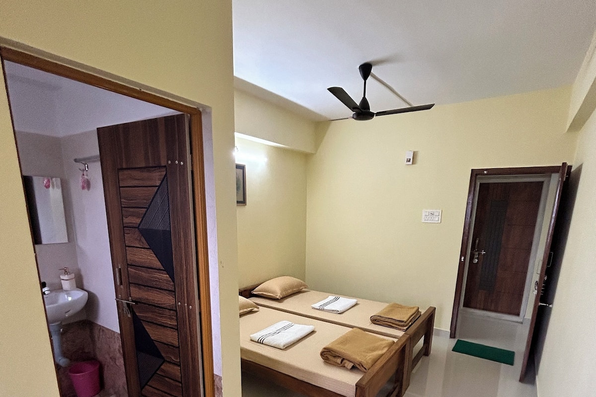 A bedroom with a bed, a ceiling fan, and a bathroom with a sink and mirror.