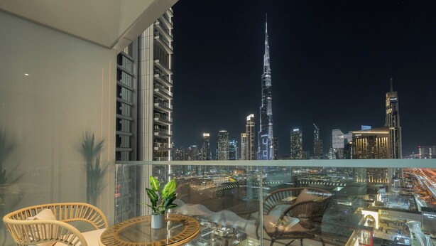 A balcony with wicker furniture, a glass table, and a potted plant. The view includes the Burj Khalifa and other Dubai skyline buildings. - Vida Dubai Mall Balcony with Burj & City Views – Walk to Dubai Mall by Heaven Crest Vacation Homes (Dubai)