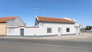 A single-story building with a tiled roof, a small porch, and a garage door. - Holiday Home 'D´Aldeia' with Shared Terrace, Private Garden and Wi-Fi (Cela Velha)